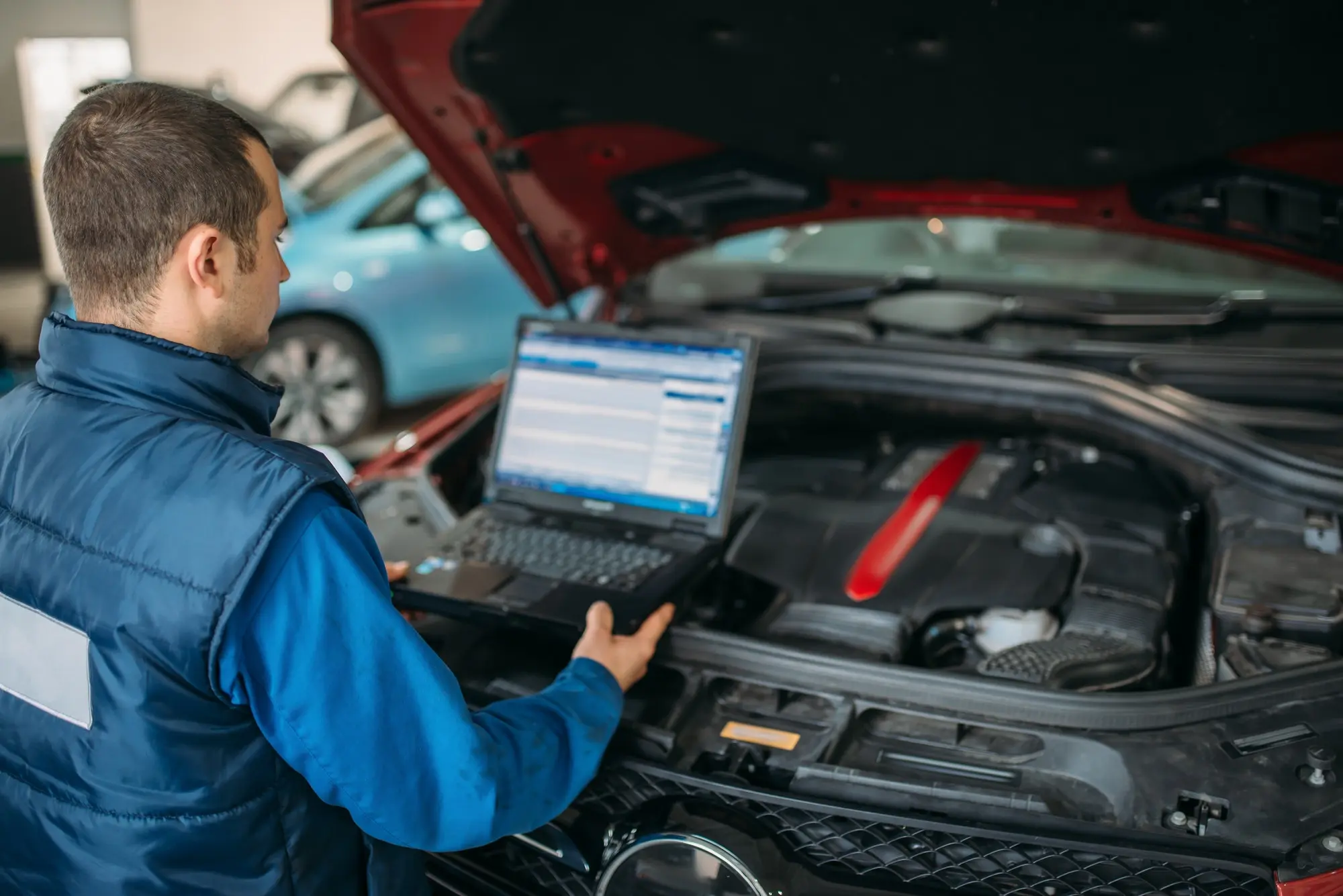 Mechanic running laptop diagnostics on car engine. Southwest Muffler & Brake, Stafford and Houston.