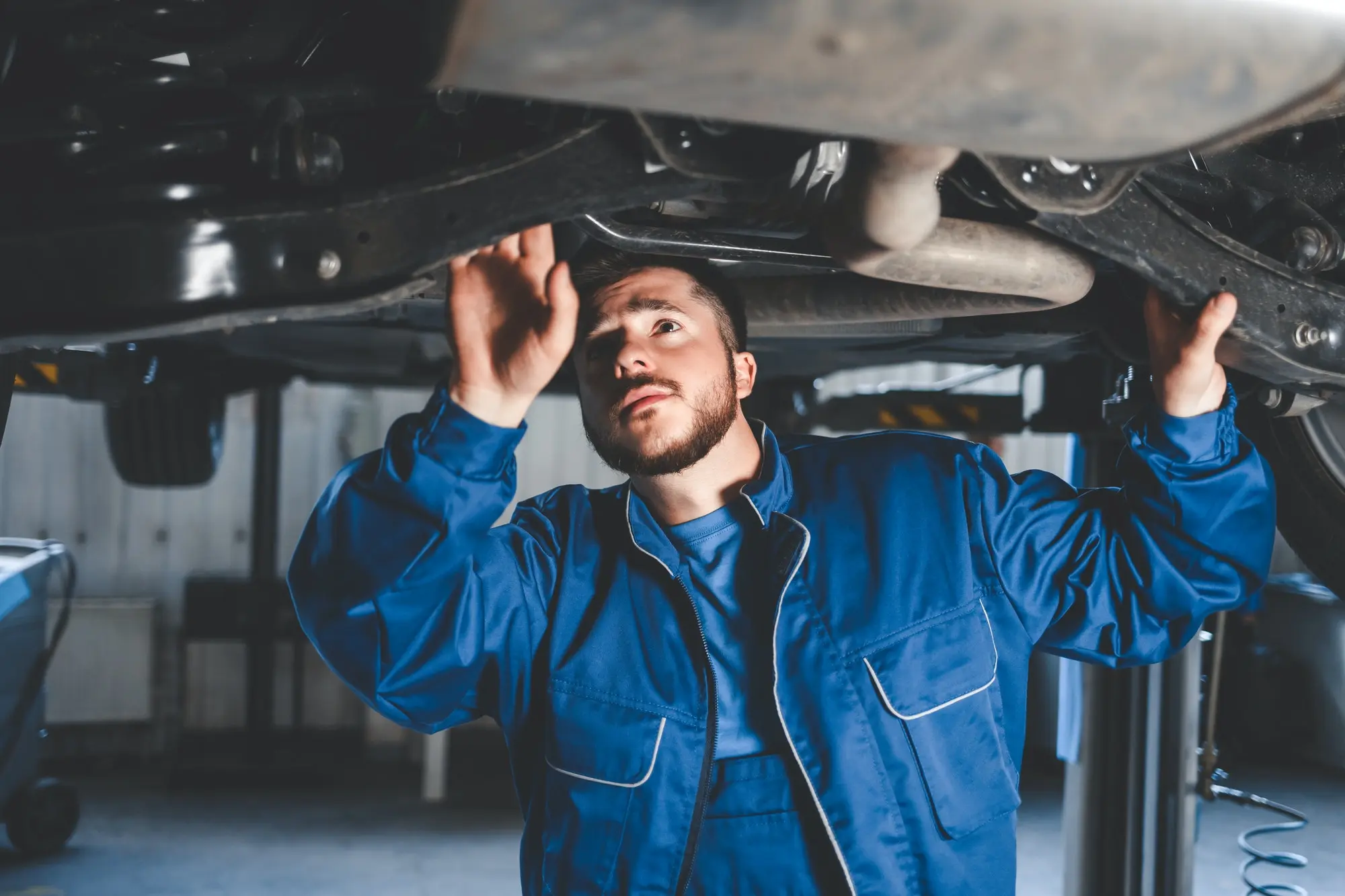 Mechanic in blue uniform inspecting car on lift. Southwest Muffler & Brake, Stafford and Houston.