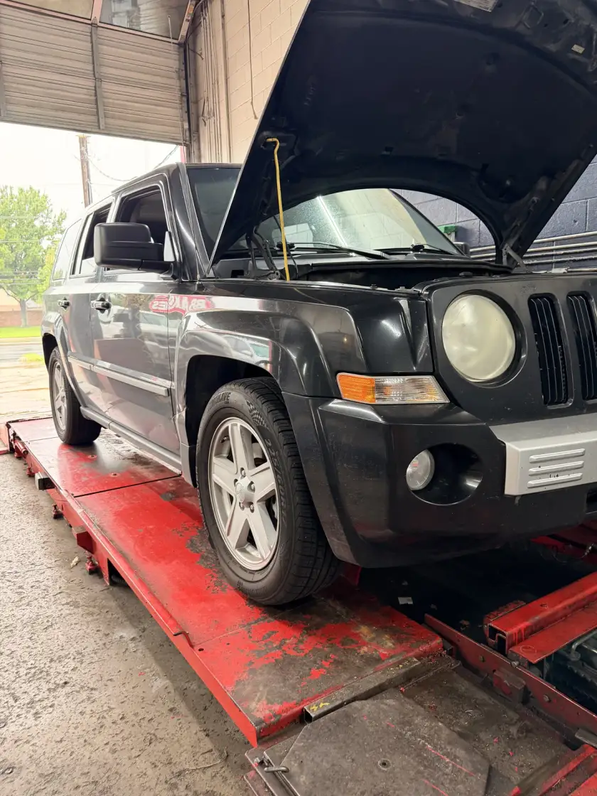 Black Jeep with its hood open on a red lift at Southwest Muffler & Brake in Houston.
