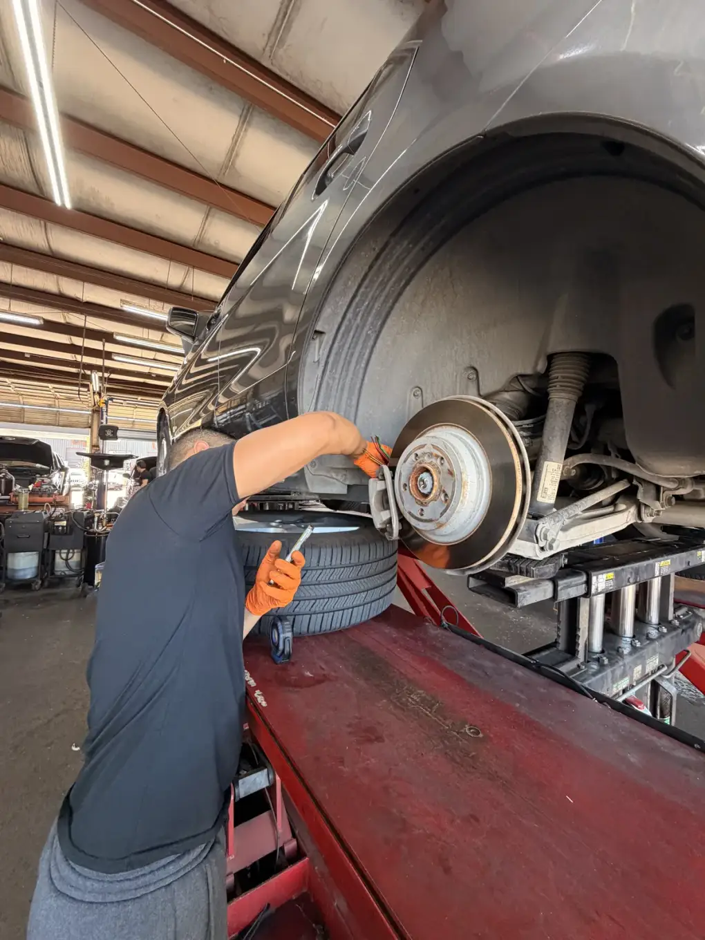 Technician working beside the exposed brake rotor of a raised car at Southwest Muffler & Brake in Stafford.