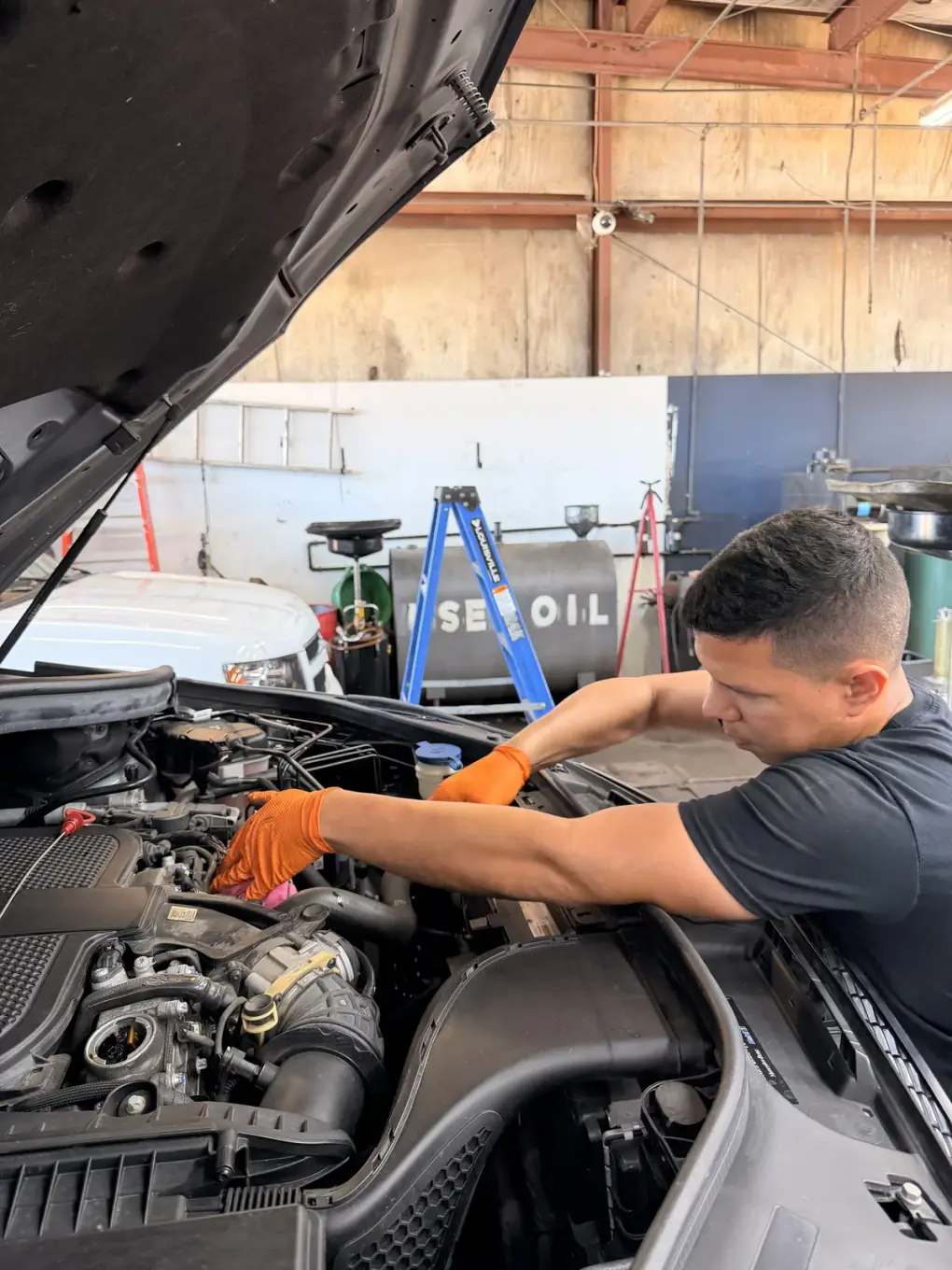 Technician wearing orange gloves working in an engine bay at Southwest Muffler & Brake in Stafford.