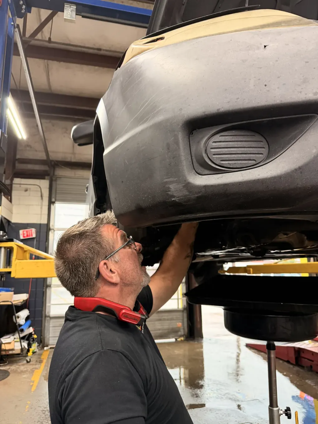 Technician working beneath a raised vehicle with a drain pan nearby at Southwest Muffler & Brake in Stafford.