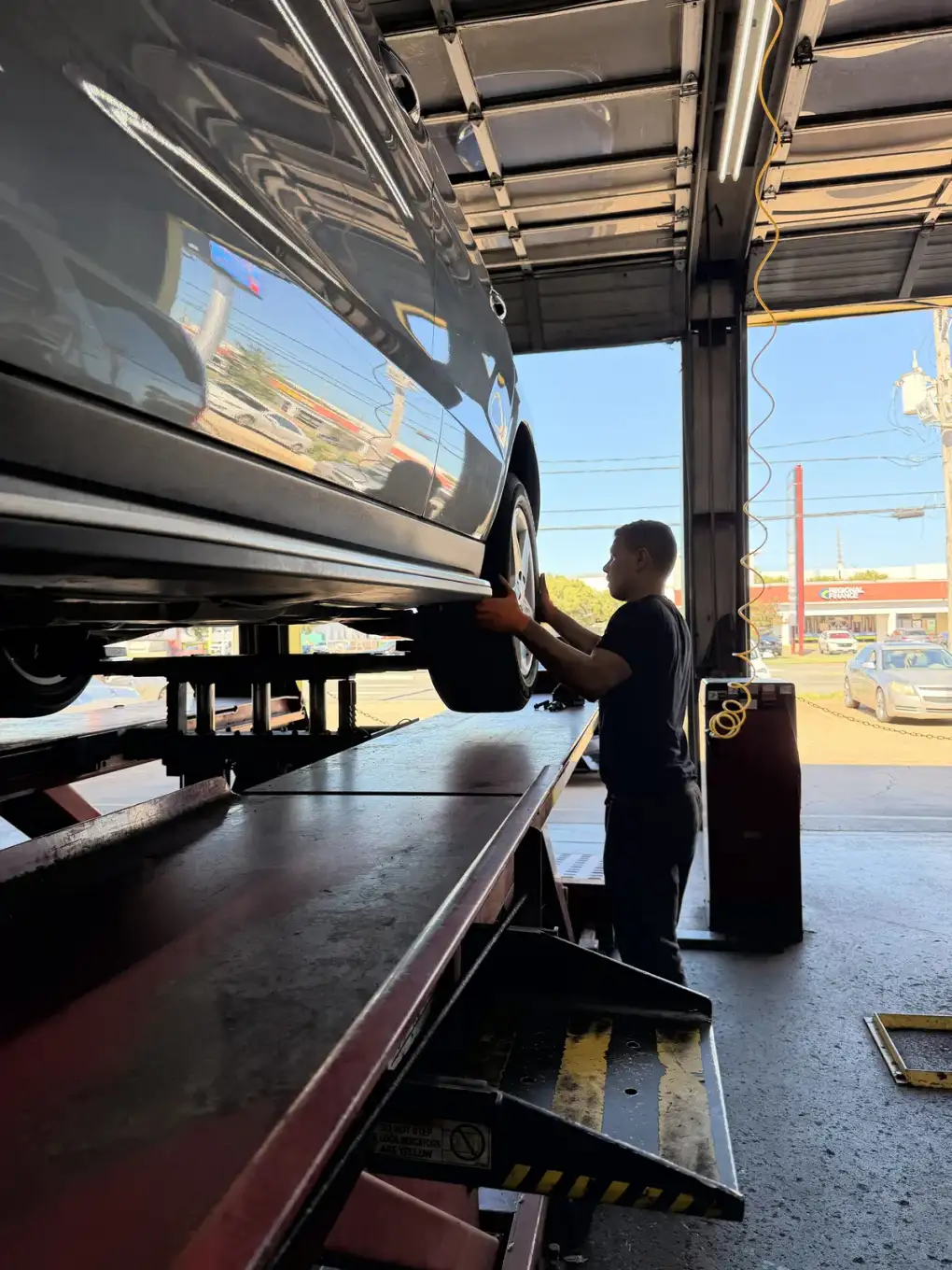 Technician working at a raised silver car beside an open bay door at Southwest Muffler & Brake in Stafford.